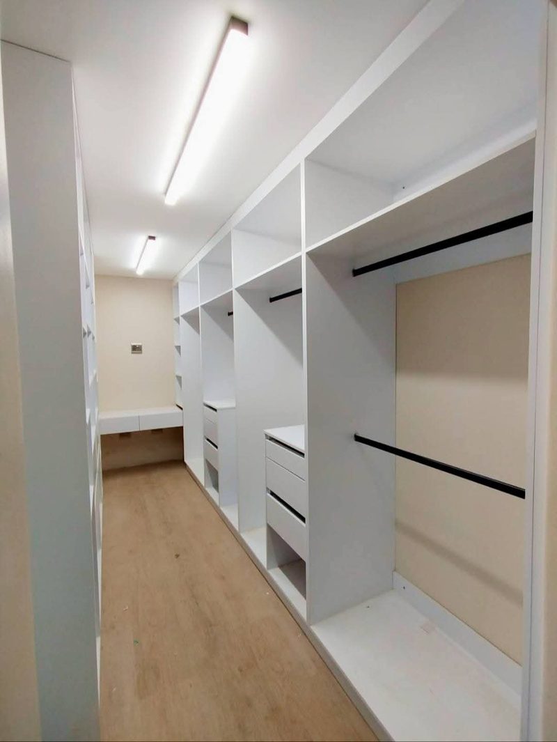 A walk-in dressing room with fitted white shelving and drawers.