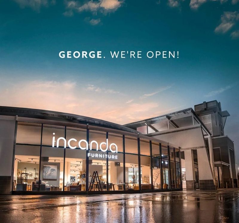 A glazed furniture showroom lit from within at dusk.