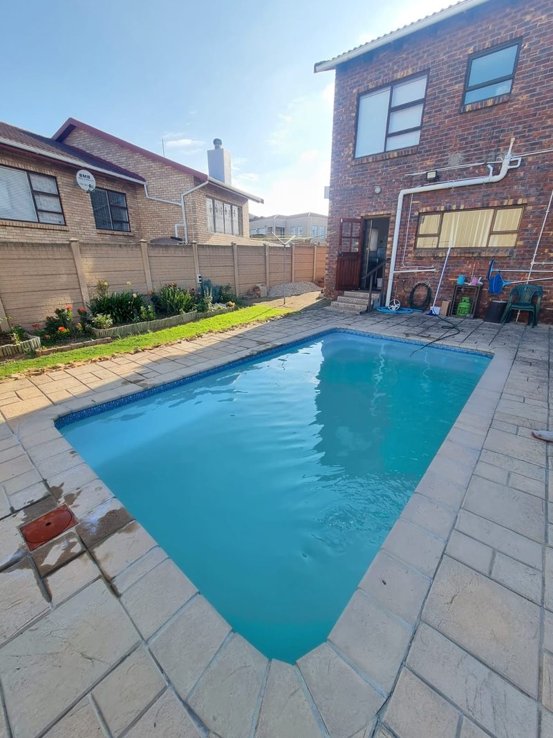 A completed swimming pool with paved surround beside a face brick house.