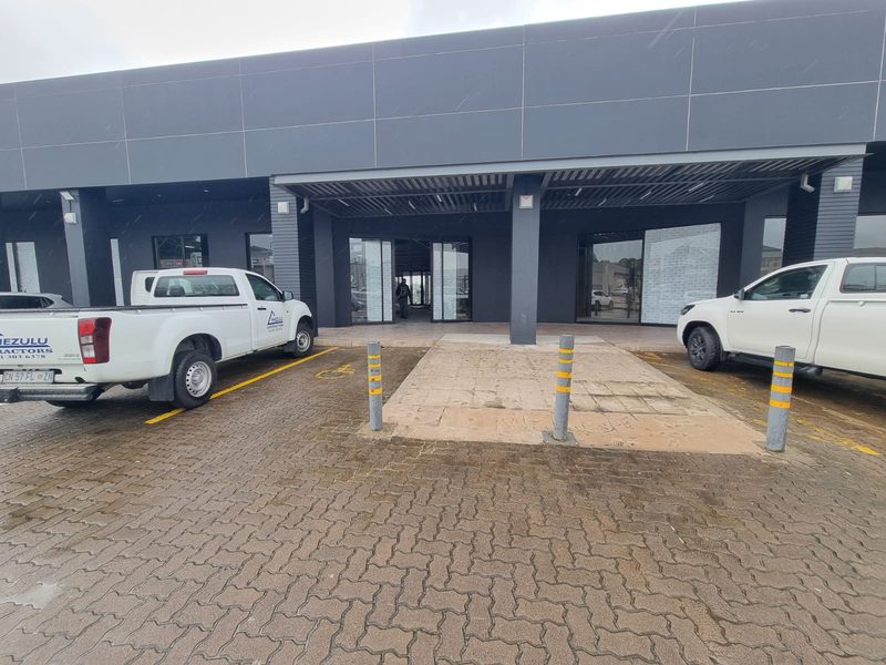 A completed dark-clad retail frontage with an entrance canopy and parking bays.