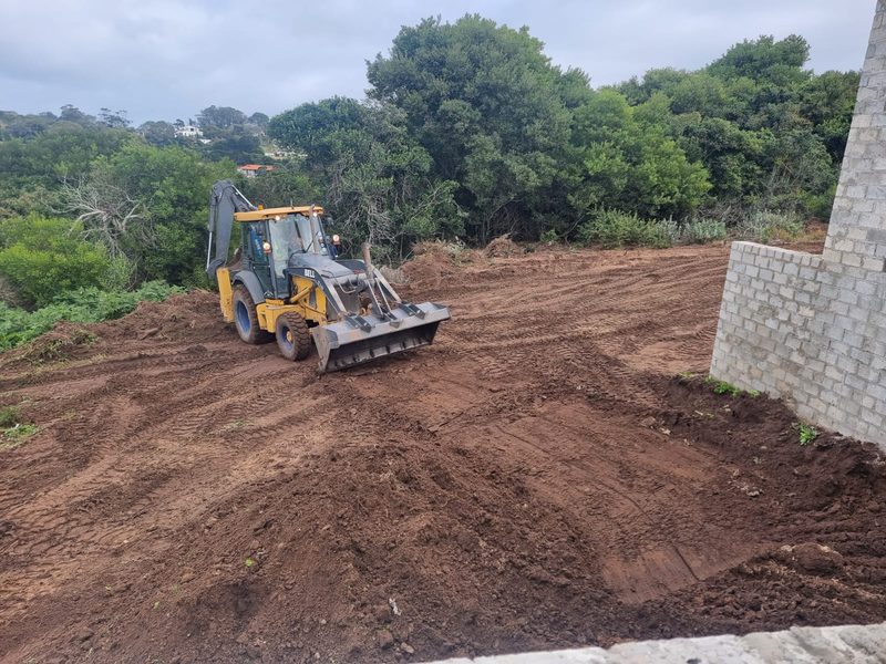A backhoe loader levelling a cleared site next to a new retaining wall.