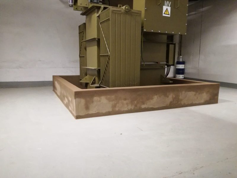 An electrical transformer standing on a cast concrete plinth and bund.