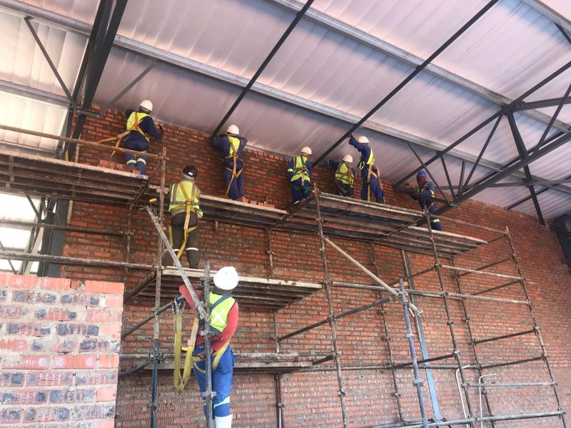 A bricklaying team working from scaffold on gable brickwork inside a steel-framed building.