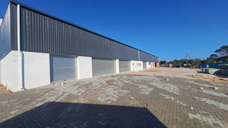 A completed clad warehouse with a row of roller shutter doors and a paved yard.